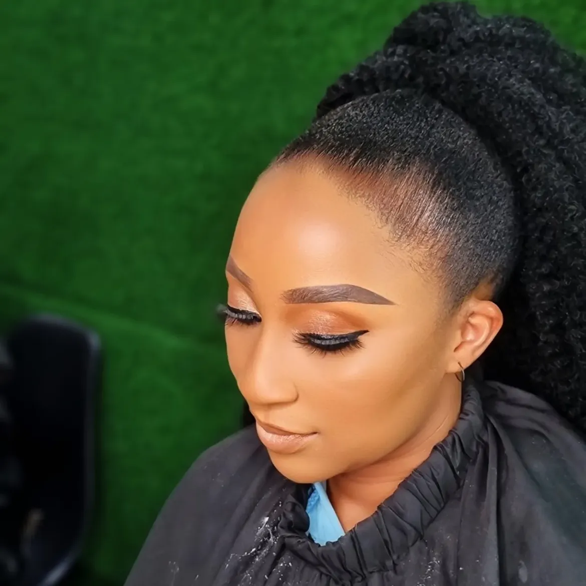 Profile close-up of sharp brow architecture, soft gold eyeshadow, and curly ponytail
