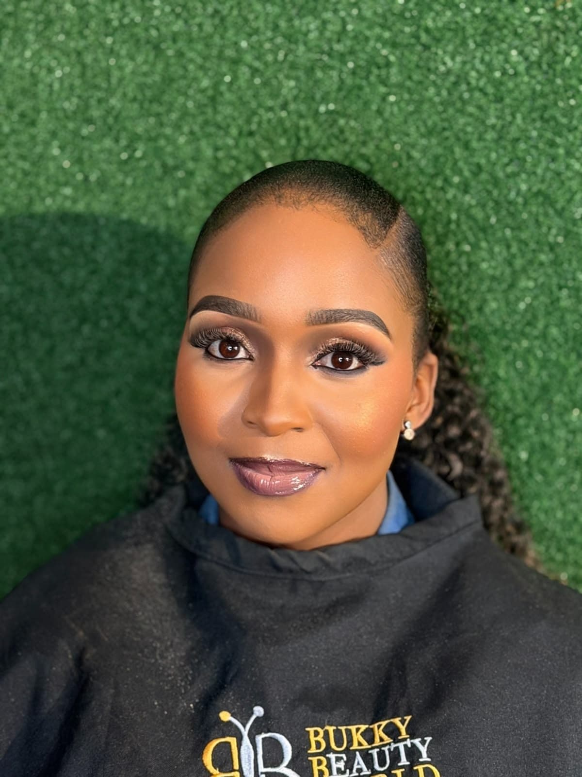 Warm amber cheek highlight, deep berry gloss, and precision side-parted sleek bun