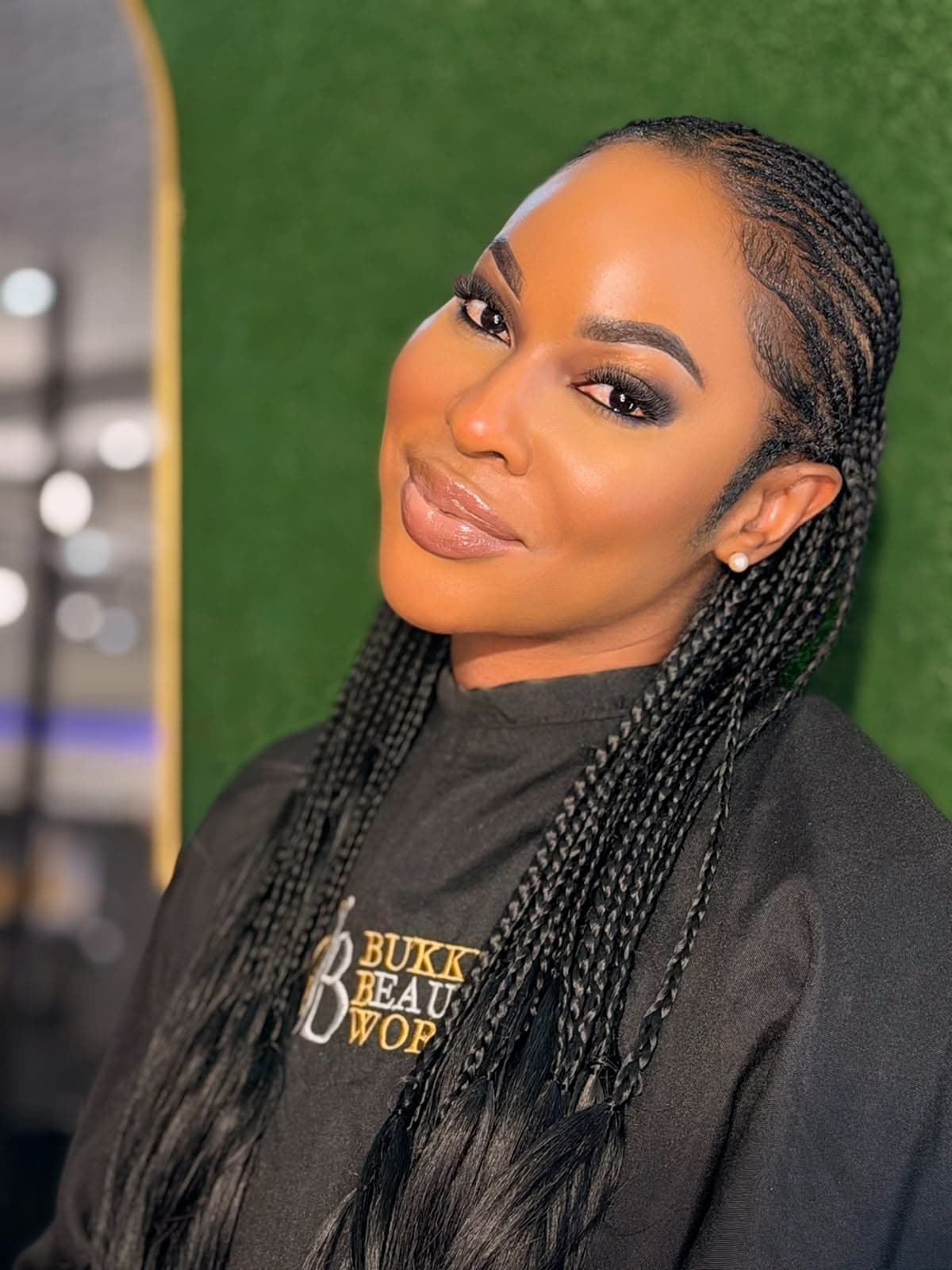 Radiant bronze complexion, precision brows, and micro-braid styling in salon cape